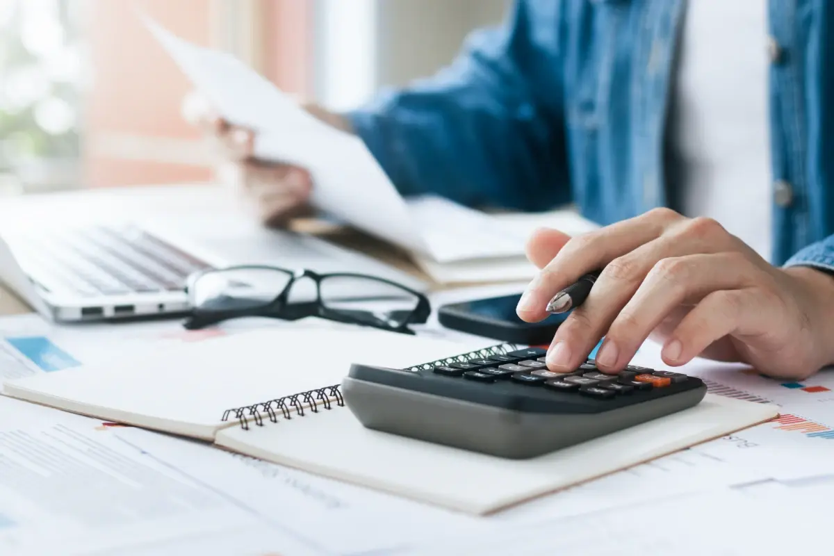 A business owner uses a calculator and reviews documents to manage finance and cash flow.