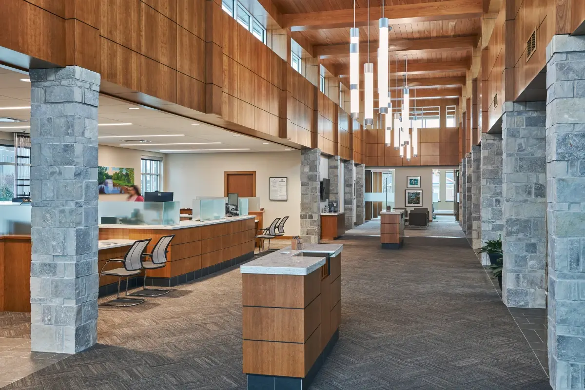 Bank First Howard location featuring stone pillars, wood paneling, and elegant cylindrical pendant lights.
