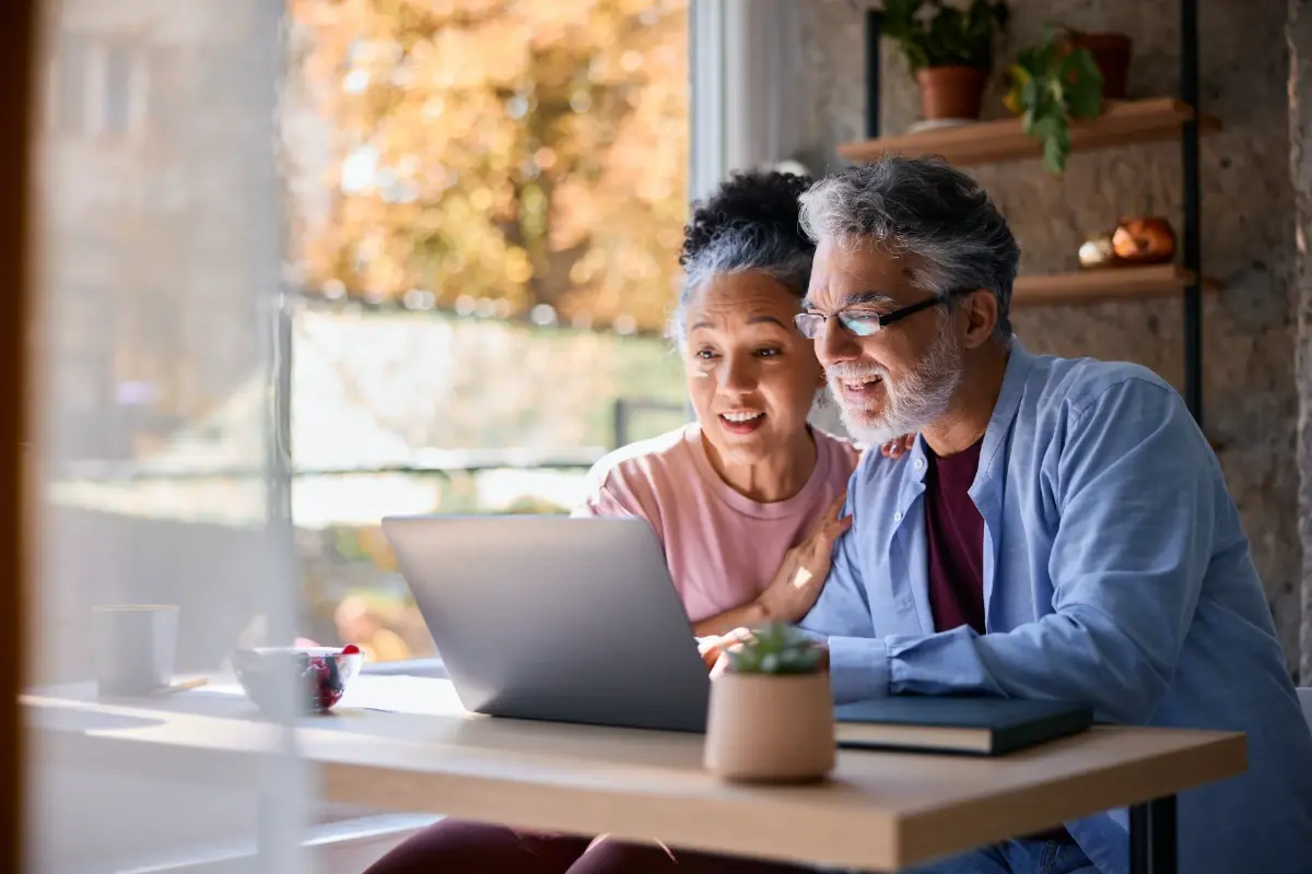 A happy senior couple looking at a laptop screen together at home.