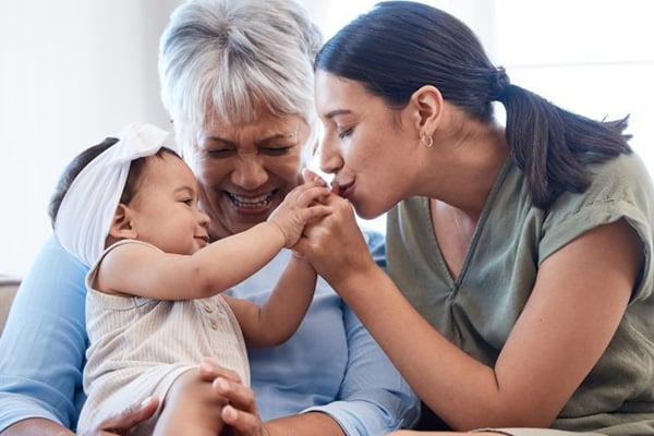 An image of a mother and daughter kissing a granddaughter's hands